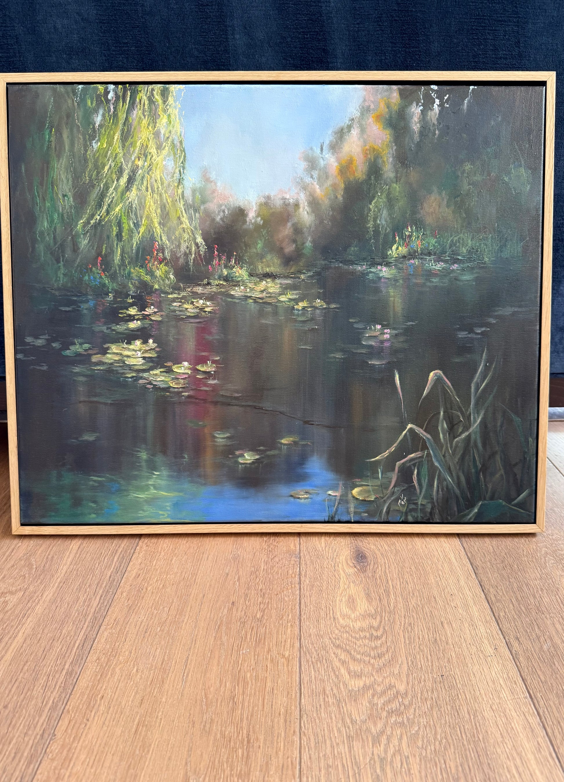 Lilies painting in floater frame, showing lily pond surrounded by willow trees. Blue sky above reflects in pond water.