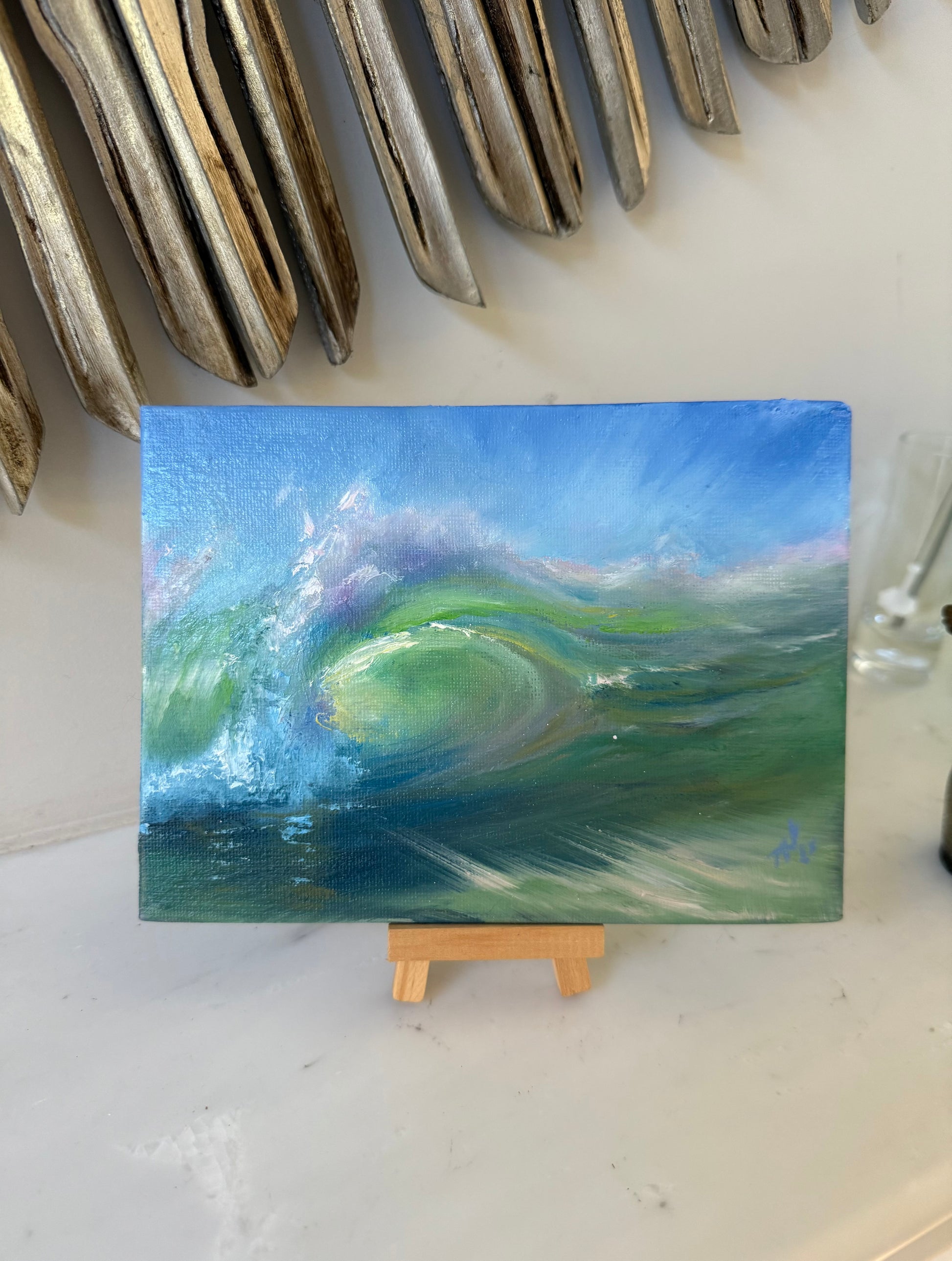 Miniature seascape, standing on a small wooden easel, showing a glowing ocean wave. Dominant colour is green.