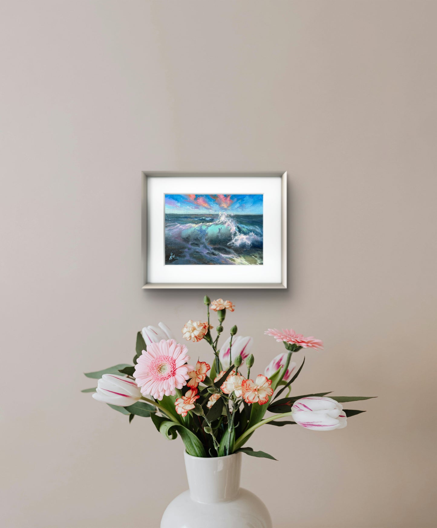 Small framed bright seascape, featuring sunset clouds and crashing waves, hanging on the wall.