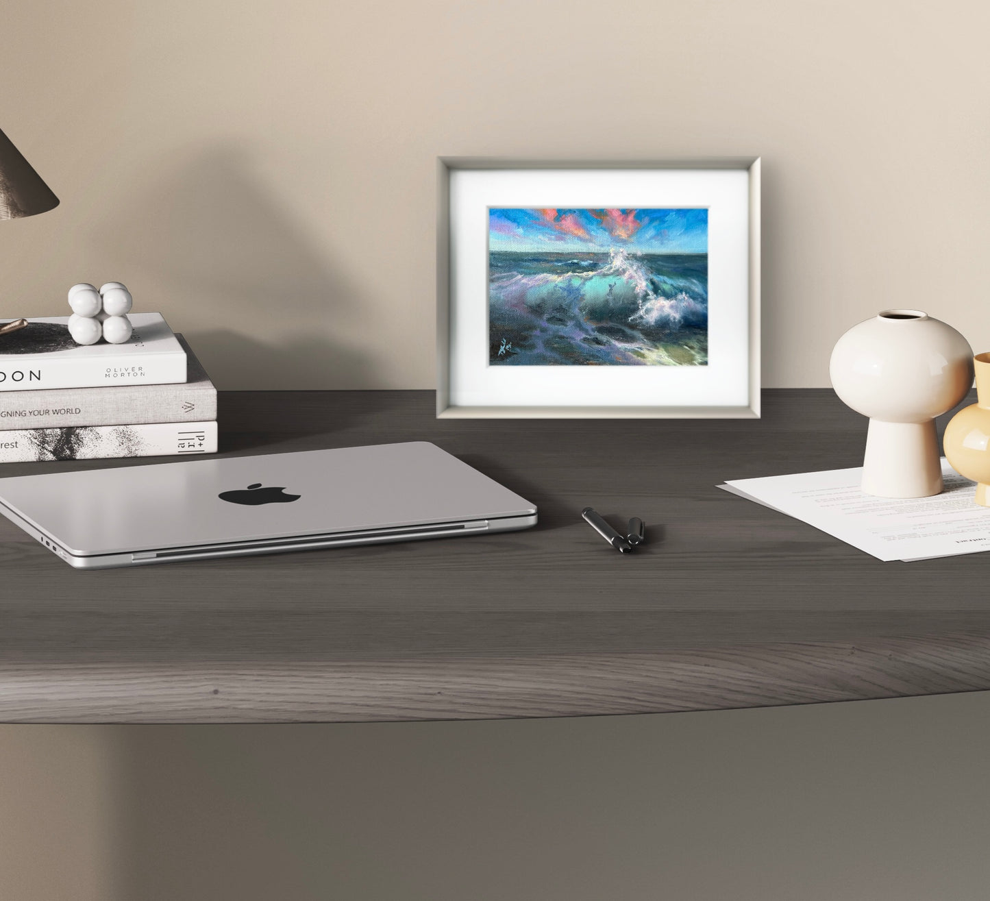 Small seascape framed in silver and white wooden frame standing on the desk top.
