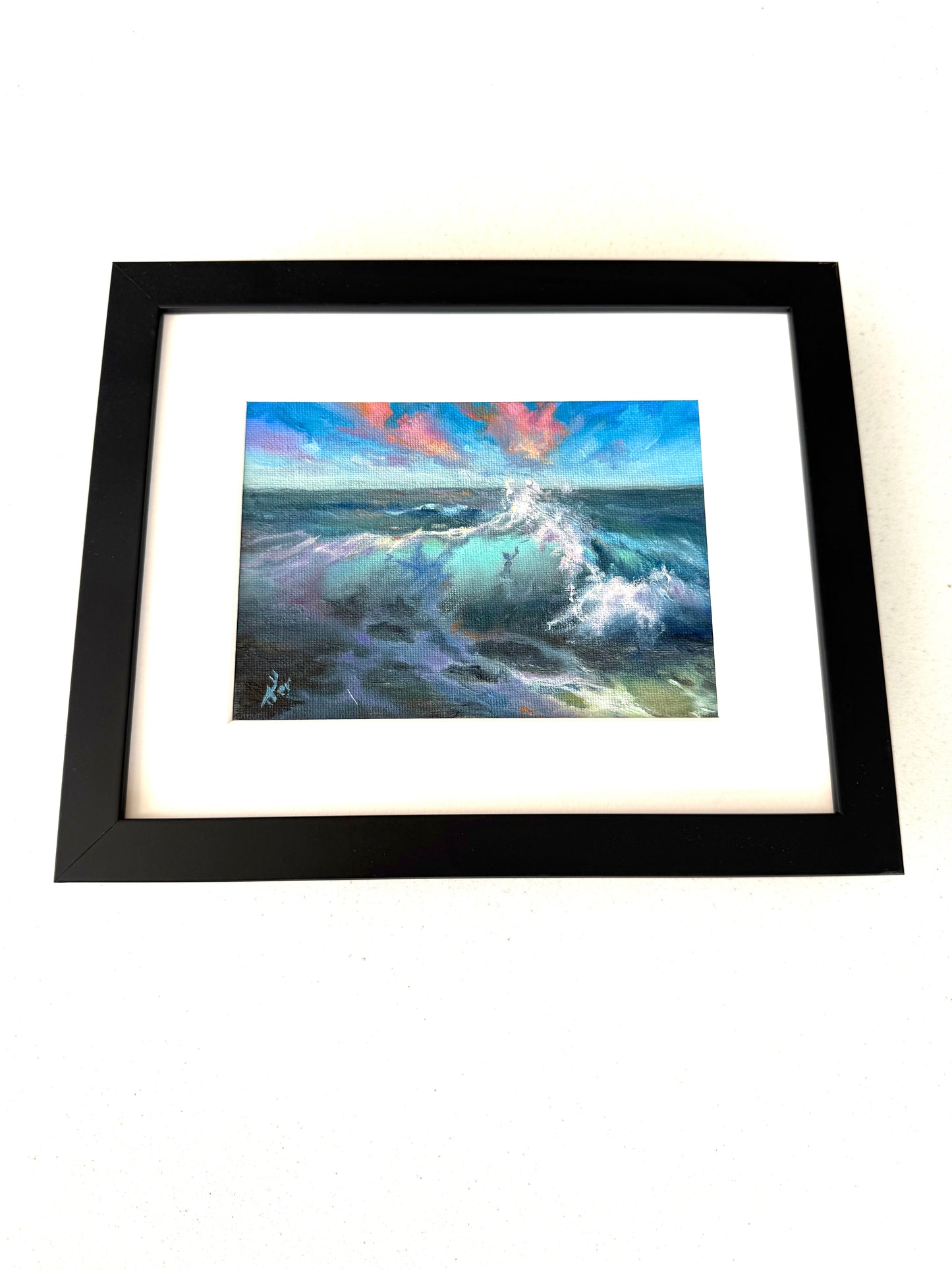 Framed in black small seascape showing turquoise wave and sunset clouds above.