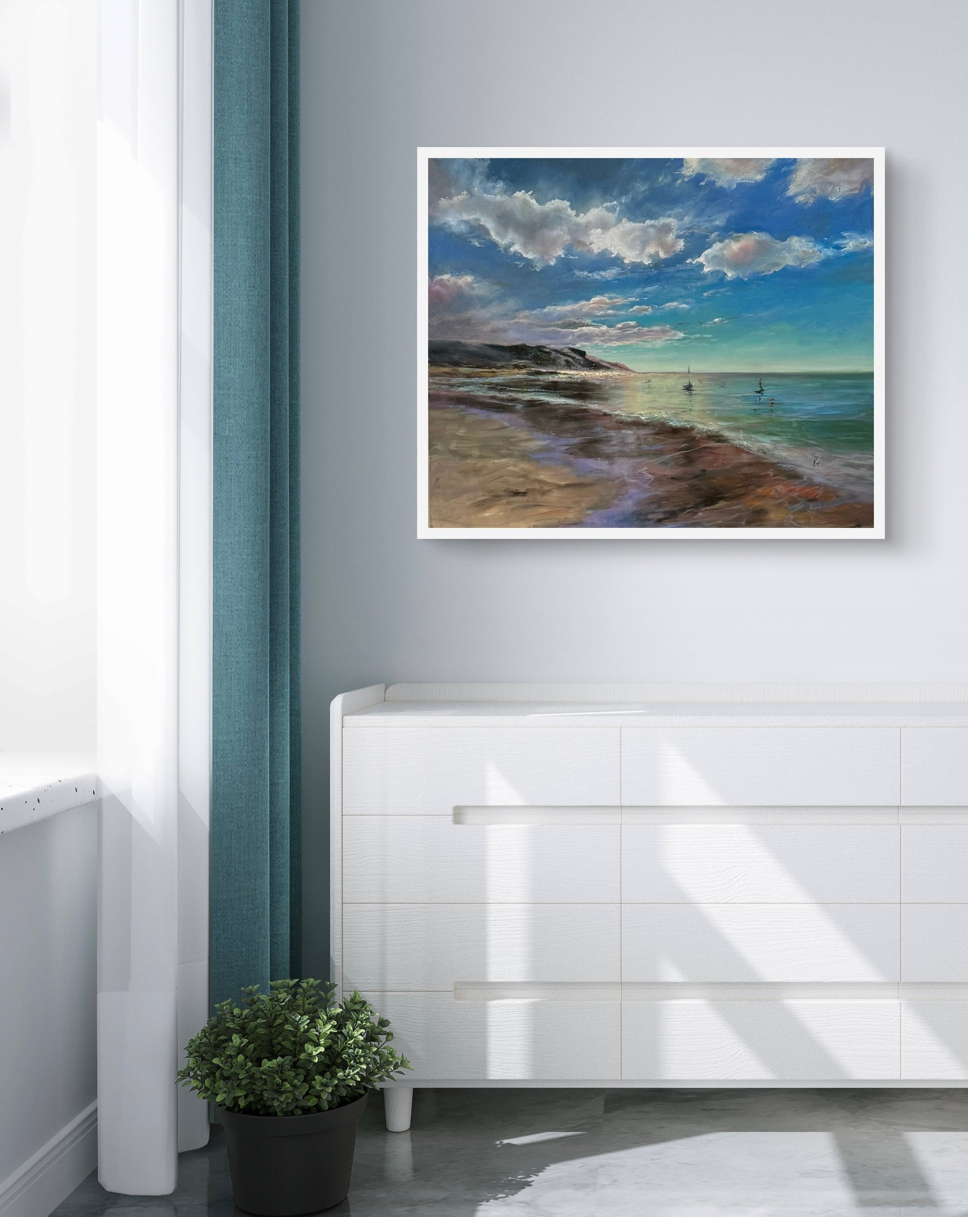 Framed beach scene painting on a wall above a white cabinet with a plant.