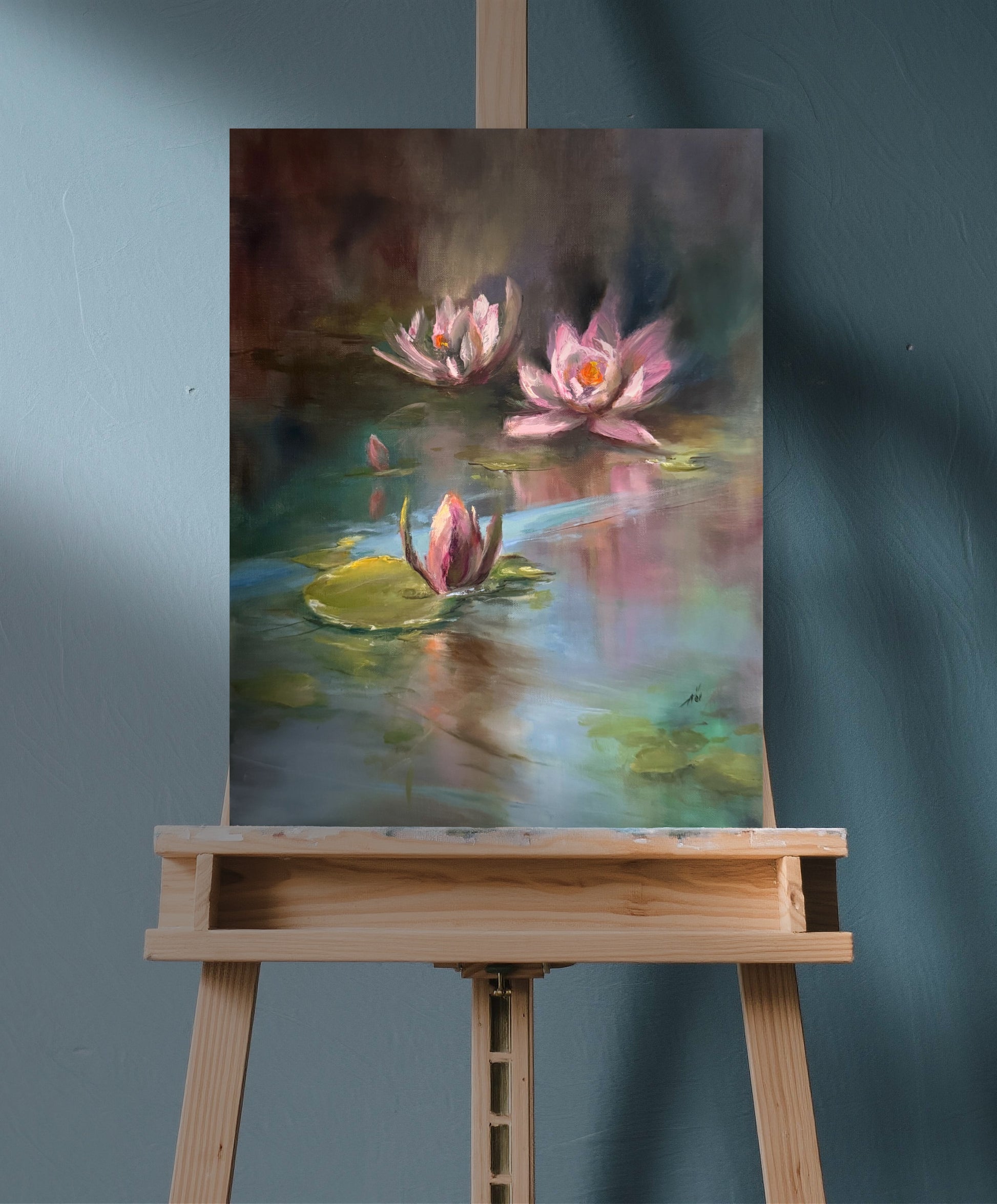 Painting of pond with pink waterlilies on a wooden easel against a teal  wall.