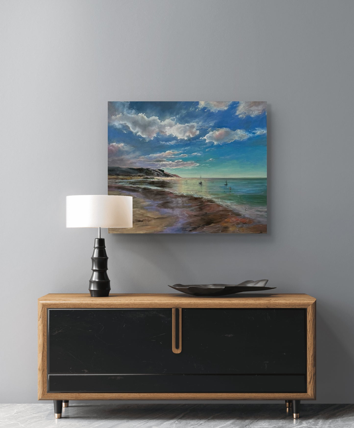 Beach scene painting above a wooden console table with a lamp and decorative bowl.