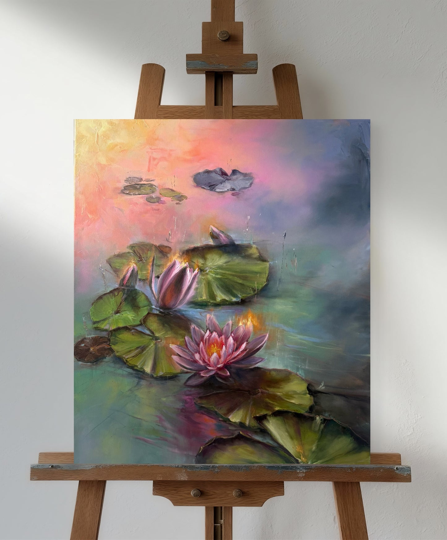 Painting of magenta and pink water lilies at sunrise on an easel against a white wall.