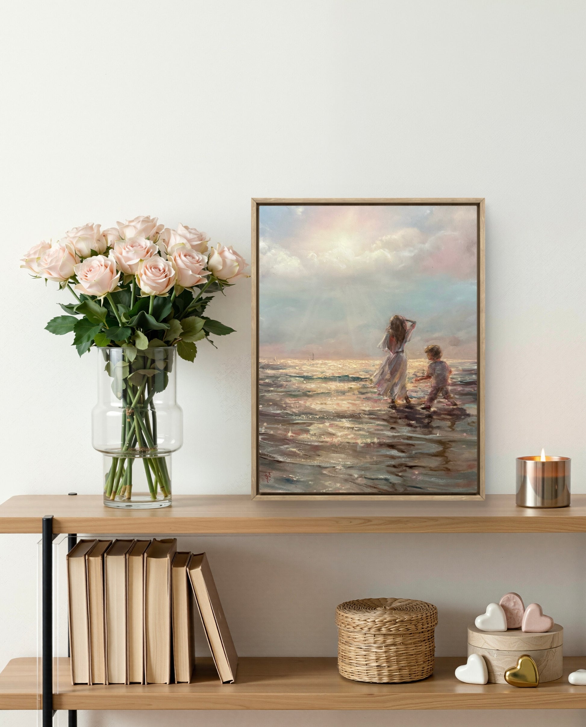 Framed waterscape artwork of children at the sunset beach on a wooden shelf with books and decorative items.