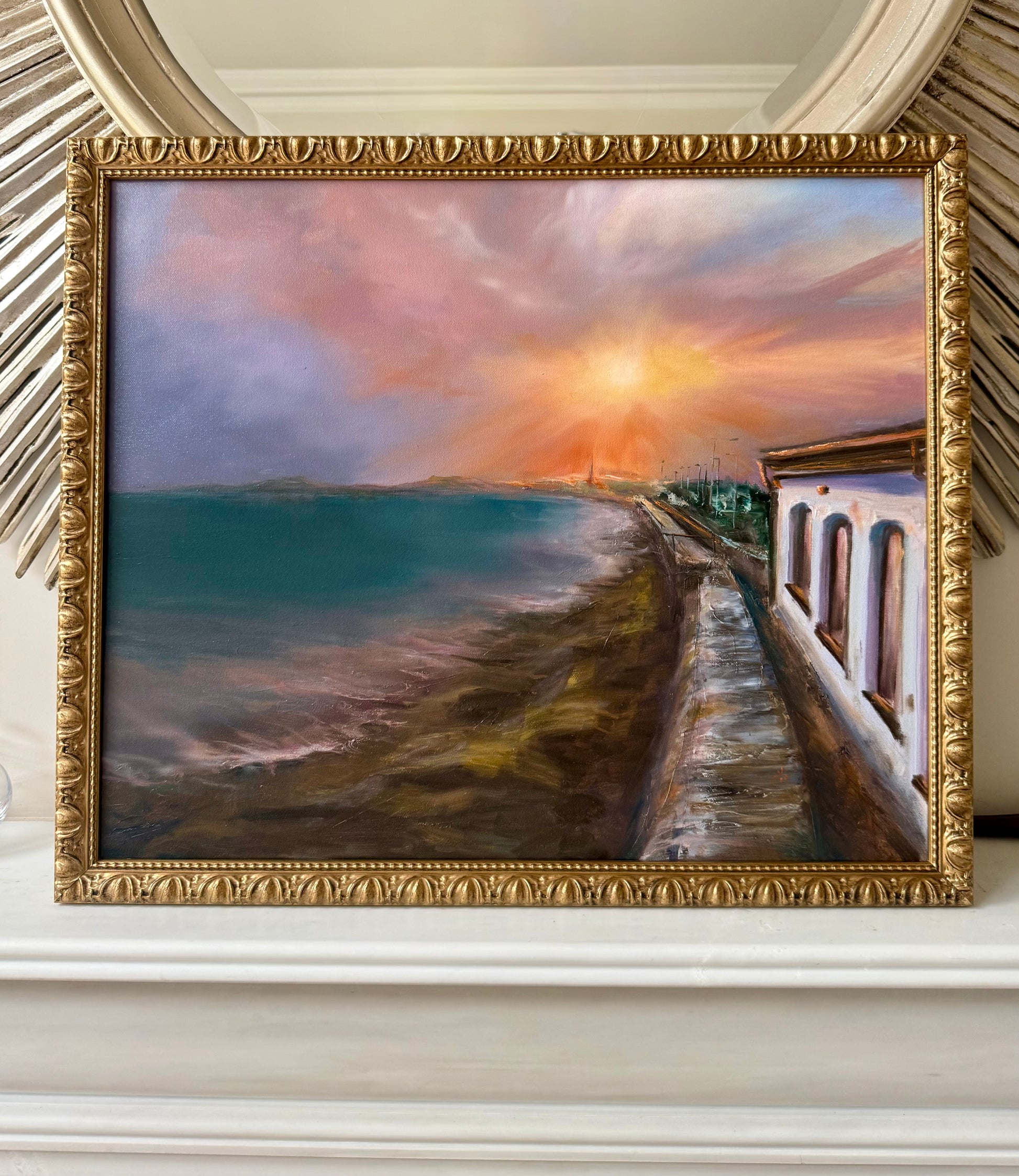 Framed painting of a coastal scene with a sunset over water.