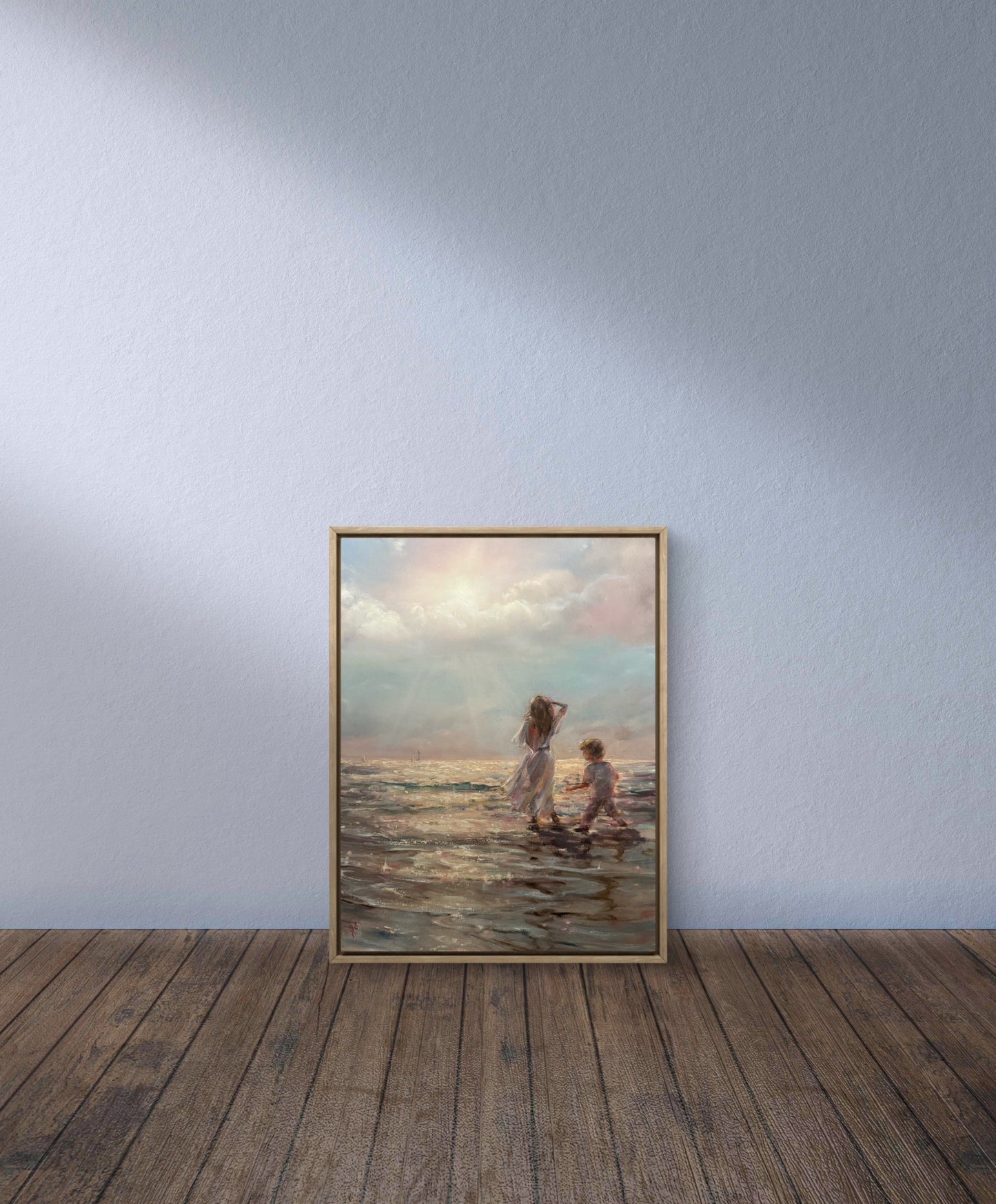 Framed artwork of two people walking along a beach on a wooden floor with a light blue wall background.