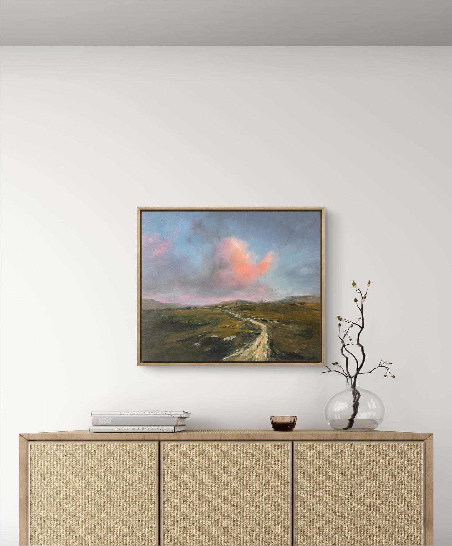 Framed landscape painting on a wall above a wooden cabinet.