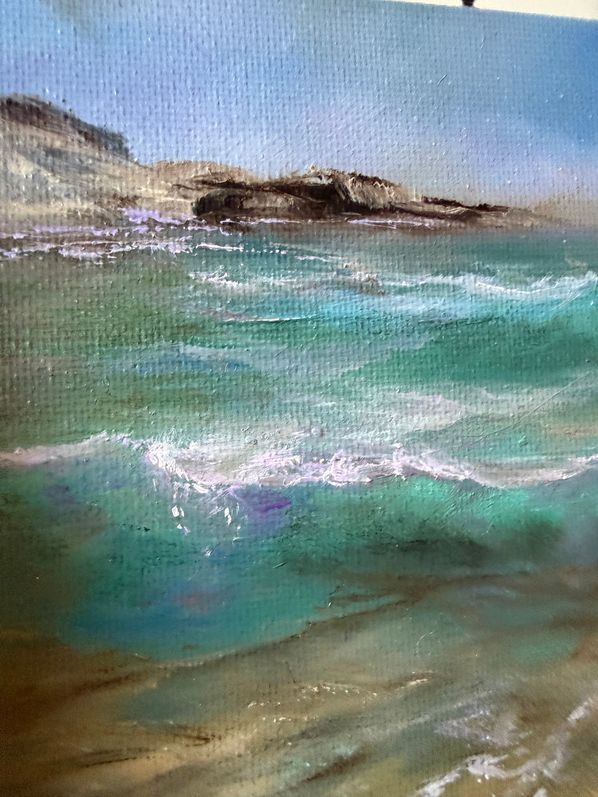 A close-up of a textured oil painting depicting a coastal seascape with turquoise and teal waves, white foam, sandy shore, and a pale blue sky.