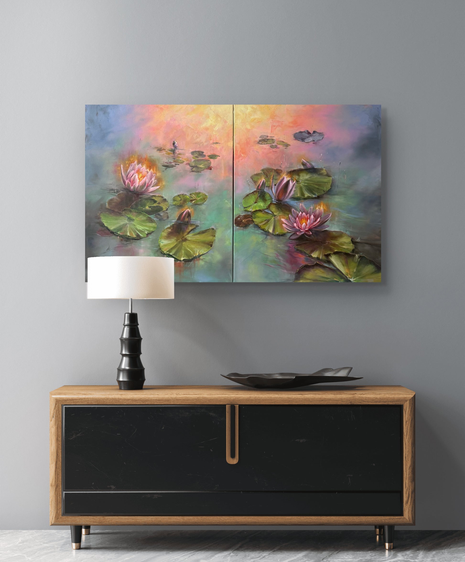 Two-panel painting of water lilies above a wooden console table with a lamp.